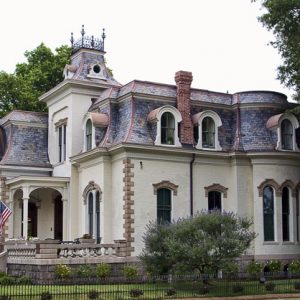 Side view of elaborate multistory house with arched windows and iron fence