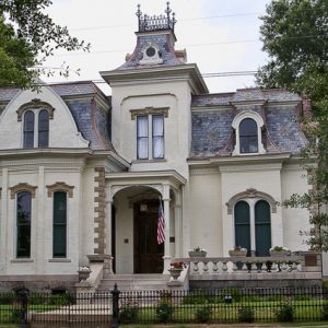 Elaborate multistory manor house with arched windows and iron fence