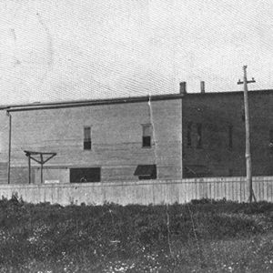 Multistory building with smoke stack in the background inside wooden fence