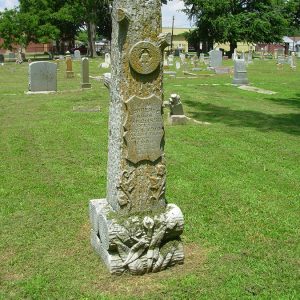 Log shaped monument in cemetery with Woodsmen of the World symbol and engraved shield on it