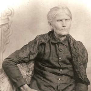 Old white woman in long sleeve button-up shirt holding an open book in her lap