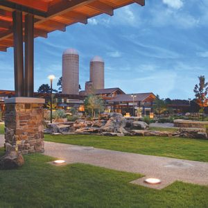 Stone fountain with street lamps and modern visitors center building with two silos from covered walkway