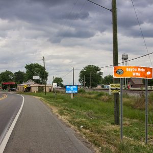 Two-lane highway through town with railroad tracks on the right side and water tower in the background