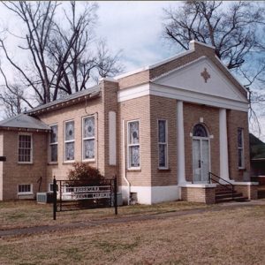 Single-story brick church building with sign and cross in front yard