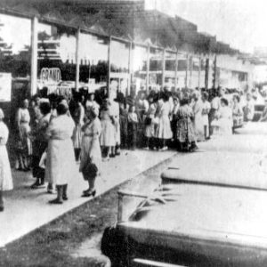 Crowd waiting outside a supermarket with parked cars