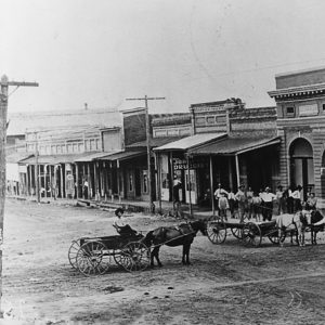 Dirt road with buildings and horse drawn wagons