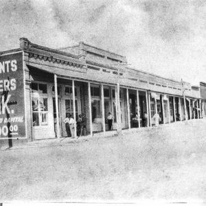 People standing at a store front with "Merchants and Farmers Bank" painted on its side