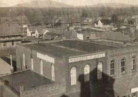 Multistory "Masonic Hall" building with houses and other structures in the background