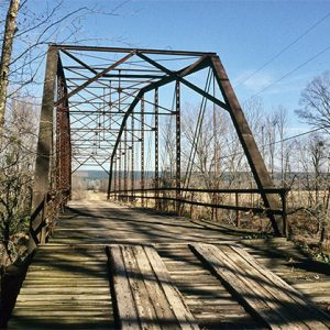 Wooden platform on steel truss bridge with railing over river and "weight limit" sign