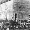 Group of white men women and children posing together outside multistory building