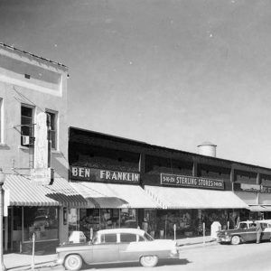 Parked cars in front of brick storefronts with awnings on street with water tower in the background