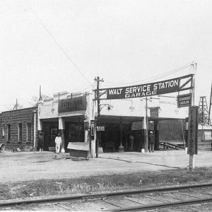 People standing before service station, water tower, car "Walt Service Station Garage"