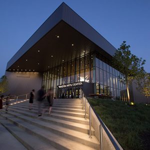 "Walton Arts Center" building with concrete steps glass covered entrance and flat roof shown at twilight with lights inside