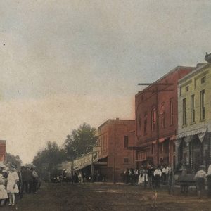 Crowd of white men women and children standing on town street with storefronts on both sides