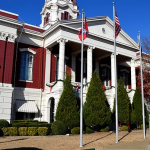 Close-up of multistory building with clock tower and covered entrance with columns and three flag poles in front yard