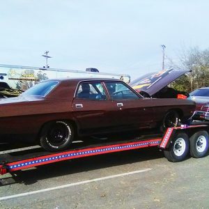 Police car and car with hood up on trailer in parking lot