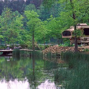 Boat dock on lake with R.V. at campsite and trees