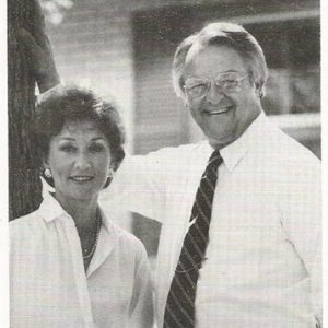 White woman with short hair and earrings smiling next to older white man smiling in shirt and tie on campaign literature