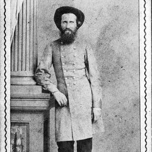 White man with long beard in hat and gray military uniform leaning on a column