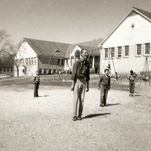 White man and boys in playground with single-story building and swing set in the background