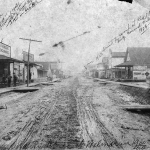 Dirt road between rows of single and multistory storefronts with covered entrances