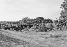 Steel suspension bridge as seen from dirt road nearby