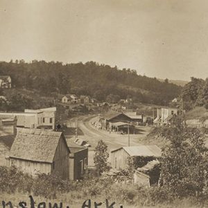 Looking over town with single-story buildings brick storefronts and multistory house in the background