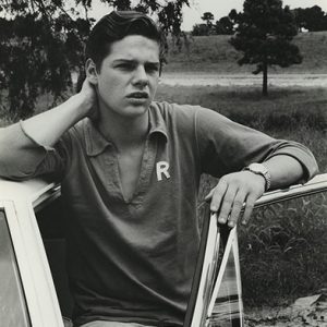 Young white man wearing "R" shirt standing at car door