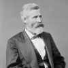 White man with beard sitting in suit and bow tie