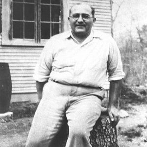 Bald white man with round glasses sitting on tree stump