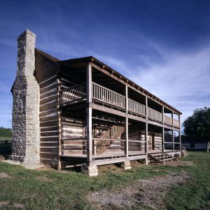 Two-story log cabin with stone chimney under blue skies