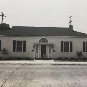 Person sitting outside single-story building on parking lot