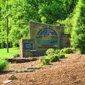 Jumping deer on stone sign with brick columns on hillside with tree next to it and trees in the background