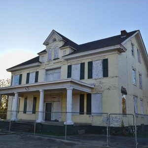 Abandoned multistory house with yellow paint behind a fence