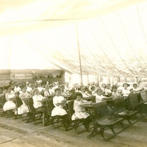 White woman speaking to class of white children in a tent