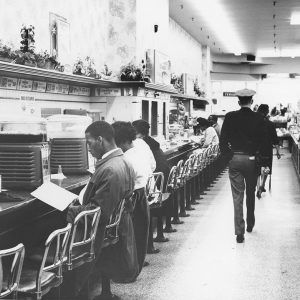 Black students sitting at lunch counter with white policeman walking by them