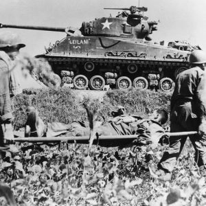 White soldiers carrying white man on stretcher with tank behind them