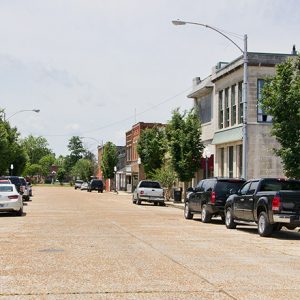 Street with two-story brick storefronts parked cars and trees