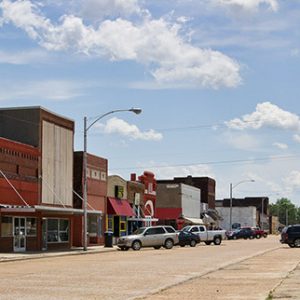 Two-story mostly red storefronts on street with parked cars and blue skies