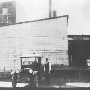 Man in suit with car outside building with smokestack and loading dock