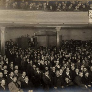 White crowd in auditorium with X-Ray banner as seen from stage