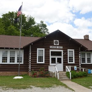 white-trimmed log cabin with flag pole and "Legion Hut" on sign above the entrance