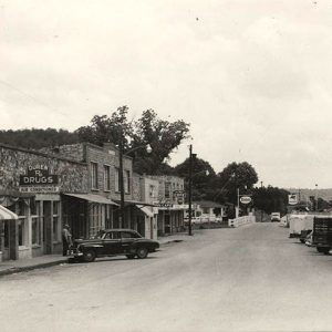 Parked cars on street across from storefronts with signs and street lamps