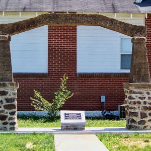 stone arch over small brick base with plaque in front of siding and brick building