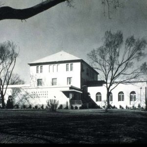 "Arkansas Childrens Hospital" sign on side of multistory building with one-story wings and large lawn winter trees by roadside