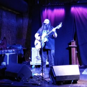 Young white man with long beard singing and playing guitar on stage