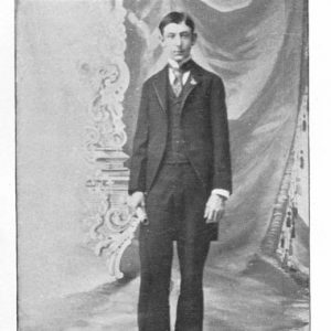 Young white man in suit and tie with curtains behind him