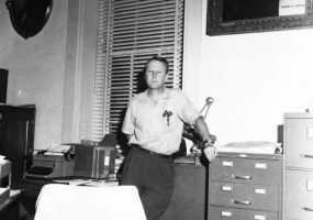 White man in a collared shirt standing in his office