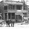 White man in a hat with horse drawn wagon pulling up to two-story building