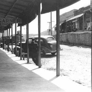 Outdoor breezeway with hanging shop signs and parked cars facing elevated street, cars, and shops